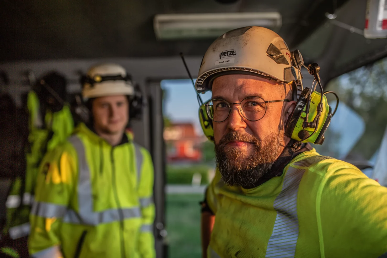 Two workers in protective gear, one focused and one blurred in the background.